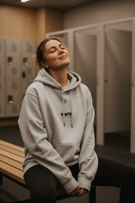 Woman relaxing in gym changing room wearing MoYB Mindful Hoodie